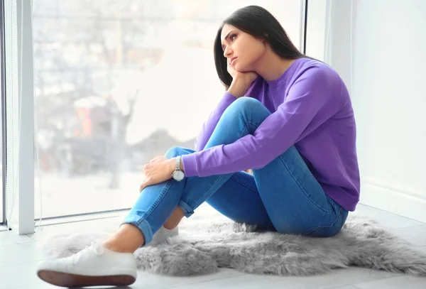 Mujer joven infeliz sentada en el suelo cerca de la ventana —  Fotos de Stock