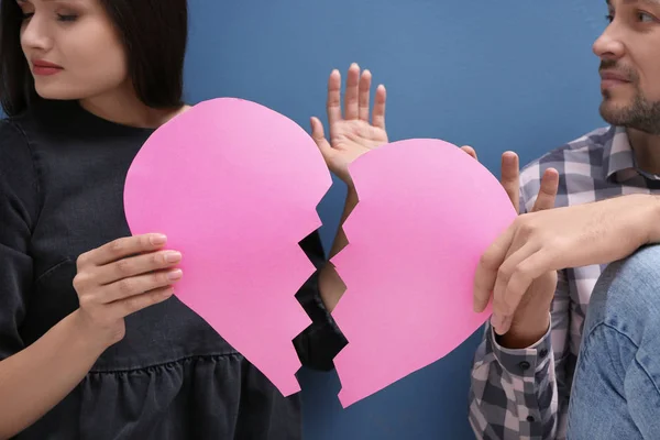 Young couple fighting while holding paper heart cut in half on color background. Relationship problems — Stock Photo, Image