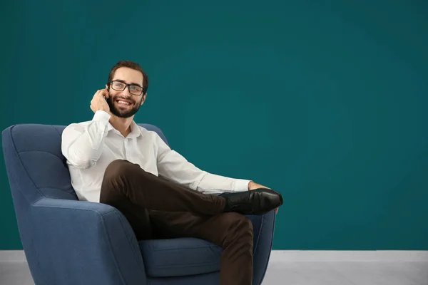 Yakışıklı adam rahat koltuk renk duvara otururken cep telefonu üzerinde konuşurken — Stok fotoğraf