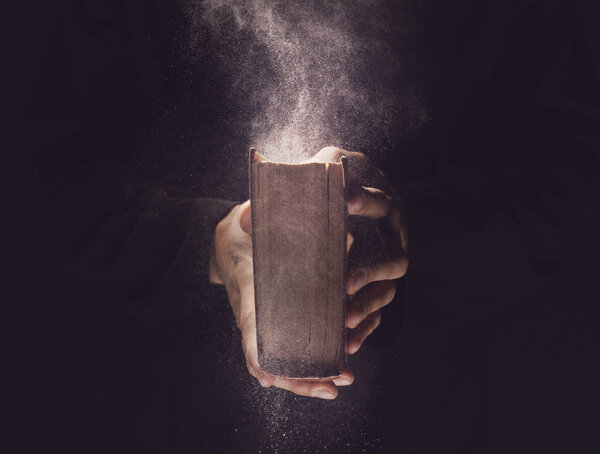 Priest with old Bible on black background, closeup