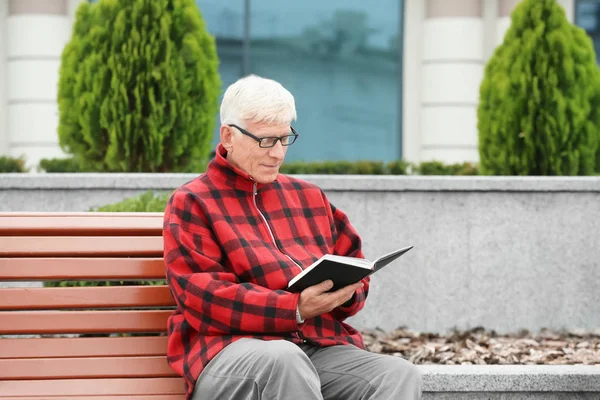 Yakışıklı olgun adam açık havada bankta kitap okuma — Stok fotoğraf