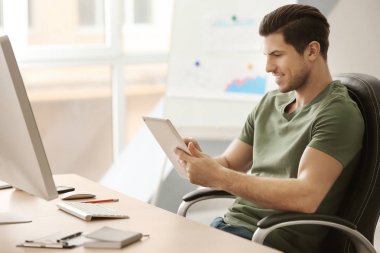 Ofiste çalışırken tablet bilgisayar kullanan genç adam