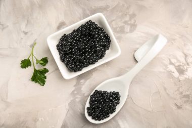Kaşık ve gri arka plan üzerinde lezzetli siyah havyar ile kase