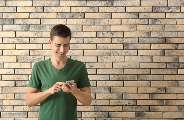 Hombre joven usando el teléfono en el fondo de la pared de ladrillo —  Fotos de Stock