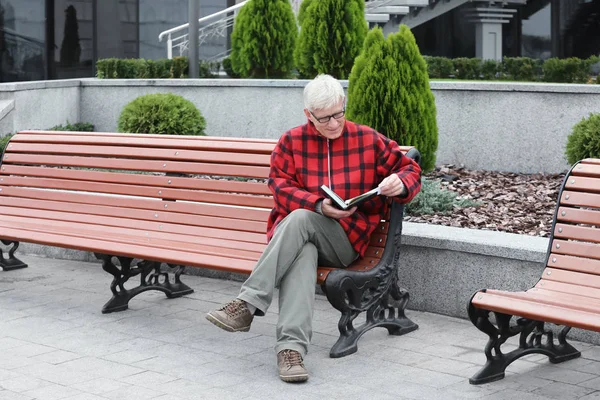 Zralý muž čtení knihy na lavičce venku — Stock fotografie