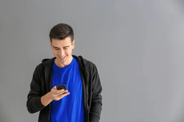 Молодой человек использует телефон на сером фоне — стоковое фото