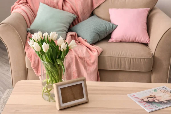 Деревянный стол с букетом тюльпанов и фоторамкой рядом с диваном в гостиной — стоковое фото