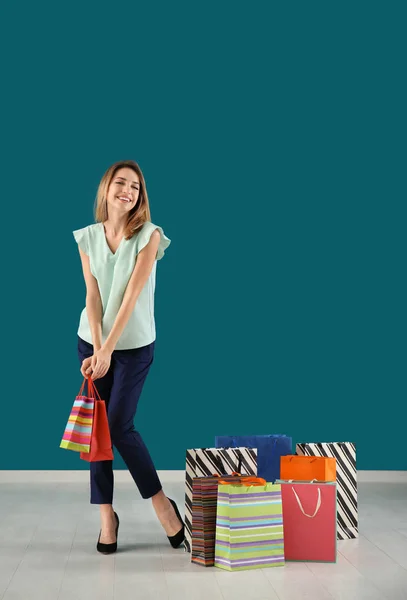 Happy young woman with shopping bags against color wall — Stock Photo, Image