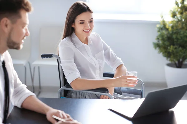 Mujer joven en silla de ruedas con colega en el lugar de trabajo — Foto de Stock