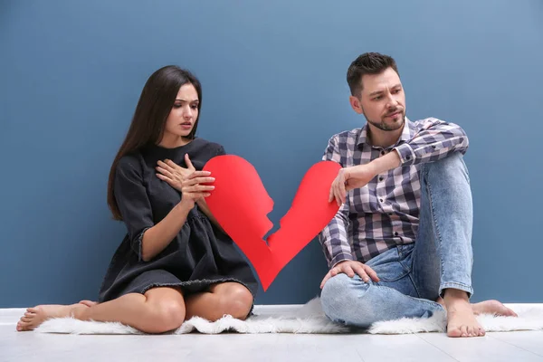 Casal jovem rasgando o coração de papel na metade perto da parede a cores. Problemas de relacionamento — Fotografia de Stock