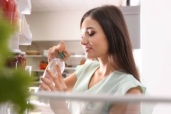 Ung Kvinna Med Flaska Vatten Nära Öppna Kylskåp Från Inuti — Stockfoto