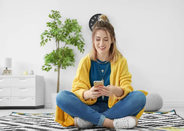 Молода жінка в жовтому кардигані, використовуючи смартфон у приміщенні — стокове фото