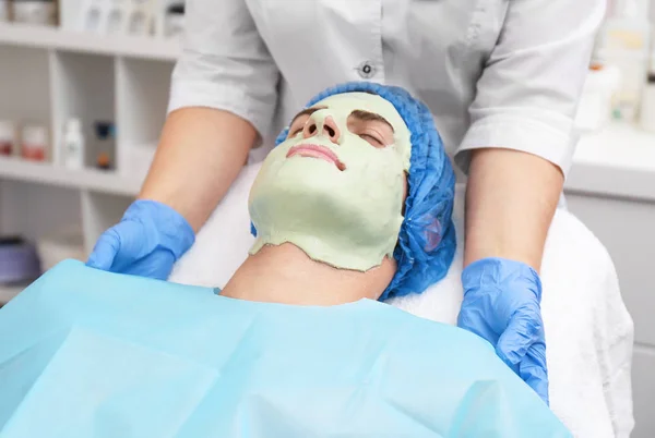 Giovane uomo con maschera facciale nel salone di bellezza — Foto Stock