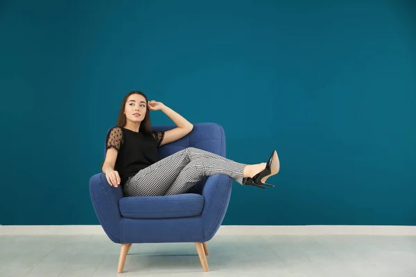 Красивая молодая женщина сидит в удобном кресле напротив цветной стены — стоковое фото