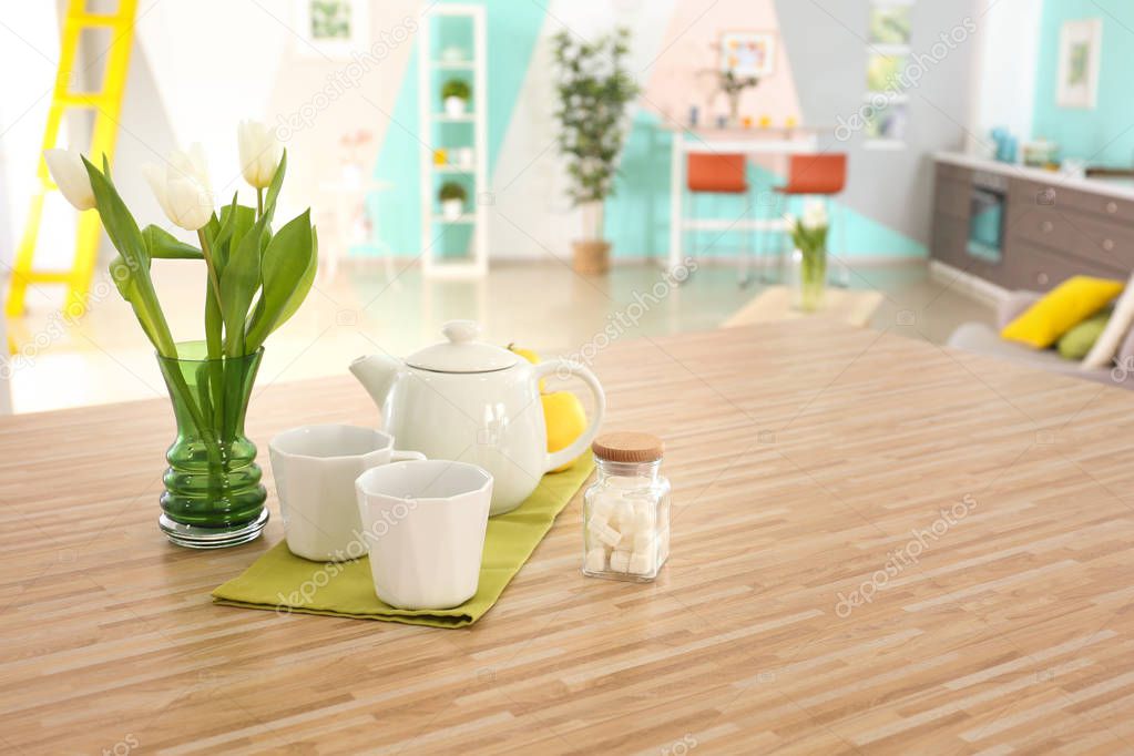 Wooden table with cups and teapot on kitchen