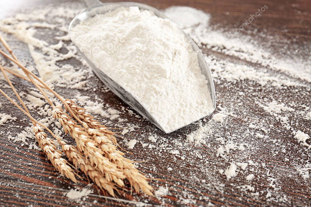 Scoop with wheat flour and spikelets on wooden table