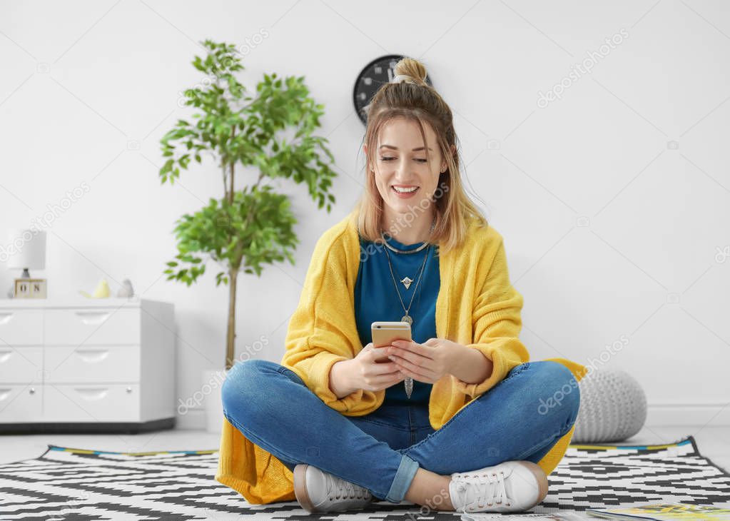 Young woman in yellow cardigan using smartphone indoors
