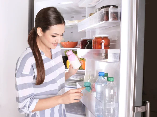 Молодая Женщина Бутылкой Йогурта Возле Открытого Холодильника Дома — стоковое фото