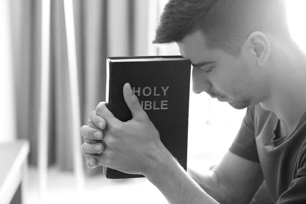 Jovem religioso com a Bíblia orando em casa, tonificado em preto e branco — Fotografia de Stock