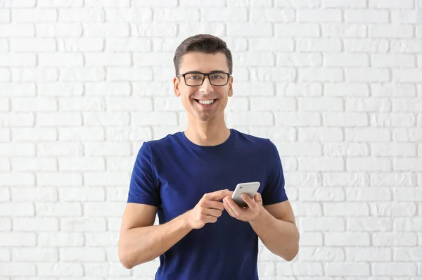 Молодой человек, использующий телефон на фоне кирпичной стены — стоковое фото