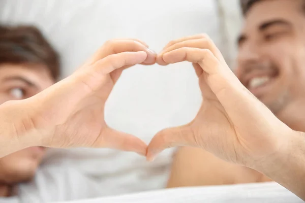 年轻的同性恋夫妇躺在床上用双手做心脏符号 — 图库照片