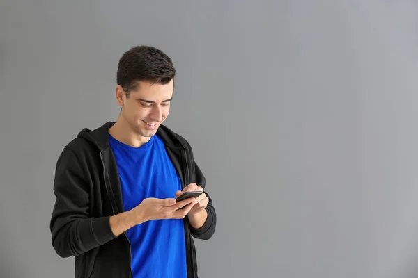 Jovem usando telefone no fundo cinza — Fotografia de Stock