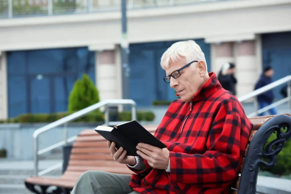 Красивий зрілий чоловік читає книгу на лавці на відкритому повітрі — стокове фото