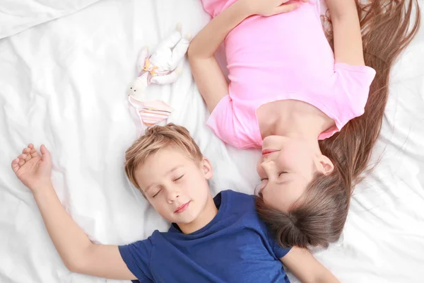 Милые младшие брат и сестра спят в постели дома — стоковое фото