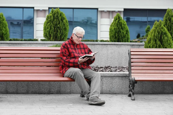 Красивий зрілий чоловік читає книгу на лавці на відкритому повітрі — стокове фото