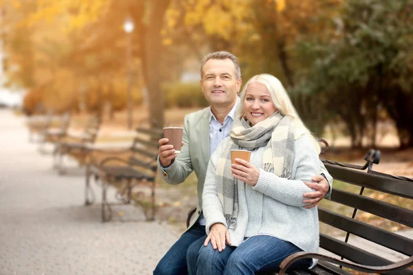 Portrait de couple mature avec café assis sur le banc dans le parc d'automne — Photo