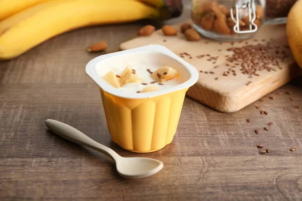 Plastikowy kubek jogurtu pyszne bananowe z nasion lnu na drewnianym stole — Zdjęcie stockowe