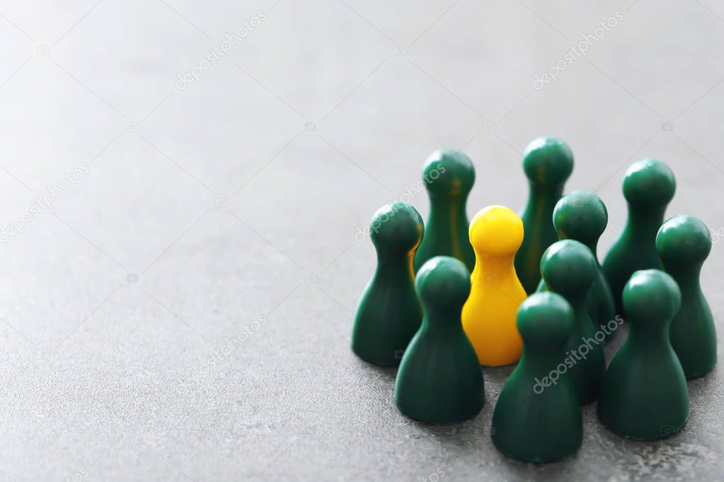 Yellow pawn among green ones on gray table. Difference and uniqueness concept