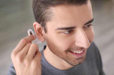 Young man putting hearing aid in his ear indoors