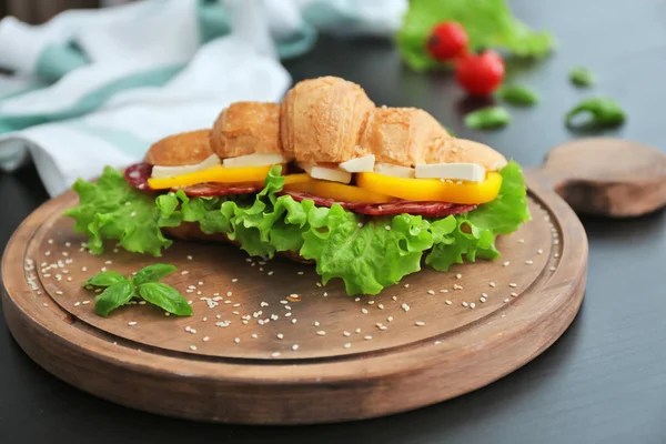 Placa de madeira com delicioso sanduíche de croissant na mesa — Fotografia de Stock