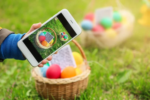 Little boy scanning QR Code in basket with colorful eggs at park, easter hunt concept