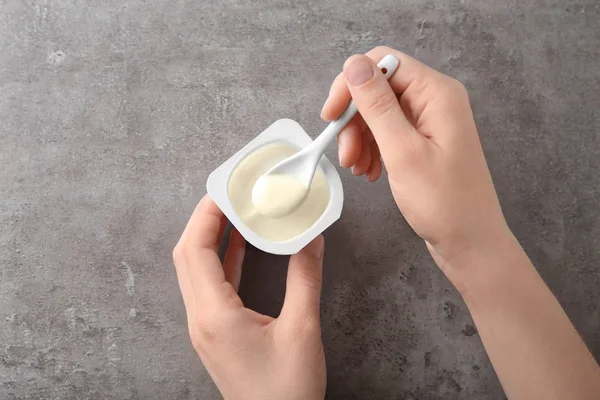 Женщина ест вкусный йогурт за серым столом — стоковое фото