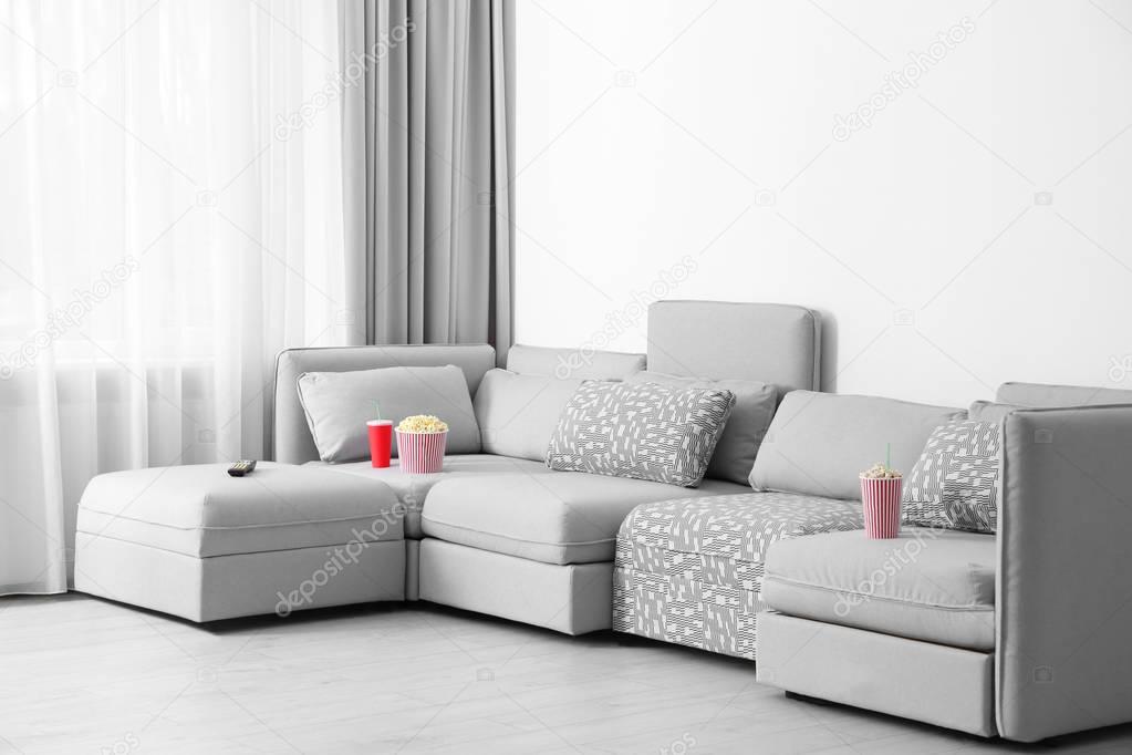 Comfortable sofa with popcorn, drink and remote control in home cinema
