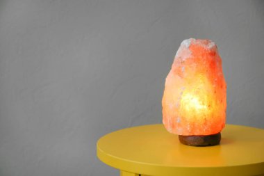 Himalayan salt lamp on table against color background clipart