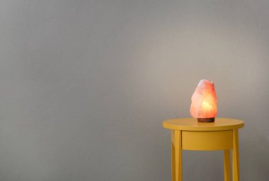 Himalayan salt lamp on table against color background clipart