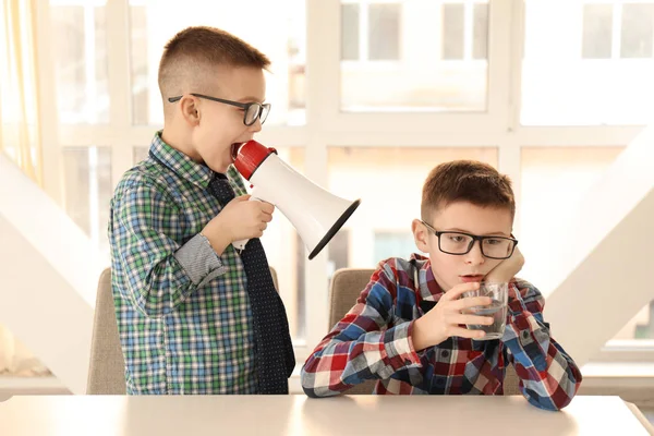 Anak kecil lucu dengan megaphone berteriak pada temannya yang bosan duduk di meja — Stok Foto