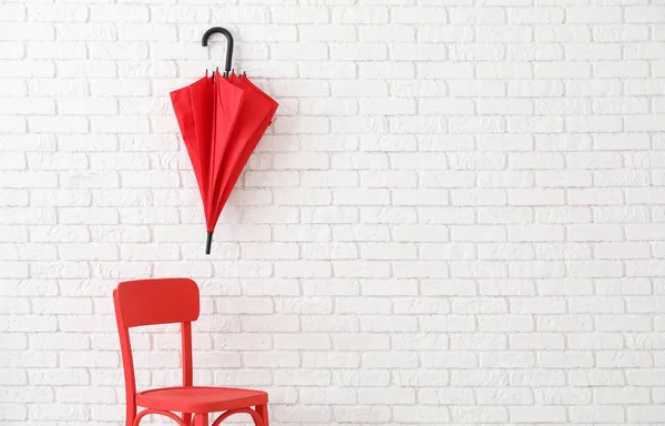 Stylish red umbrella hanging above chair on brick wall — Stock Photo, Image