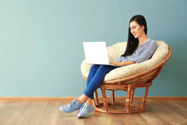 Young Asian woman using laptop in lounge chair, indoors — Stock Photo, Image