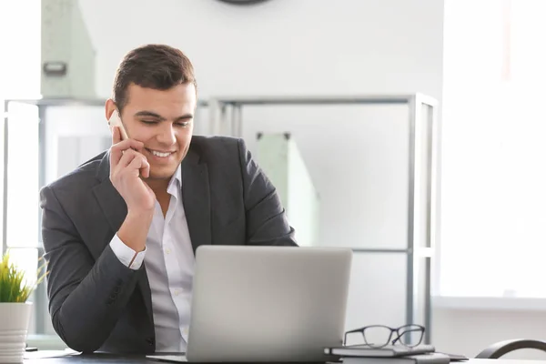 Молодой человек в офисной одежде говорит по телефону на рабочем месте — стоковое фото