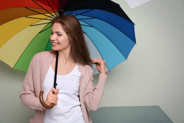 Young woman with rainbow umbrella on color background