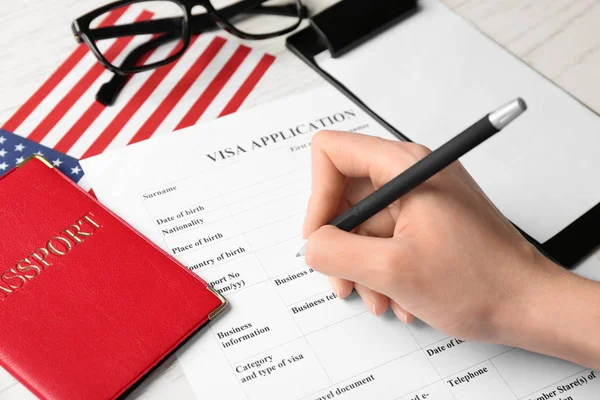 Mujer llenando formulario de solicitud de visa cerca de bandera americana en la mesa. Inmigración a Estados Unidos —  Fotos de Stock