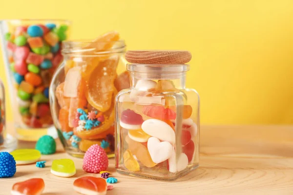 Vetreria con diverse caramelle sul tavolo contro lo sfondo di colore — Foto Stock