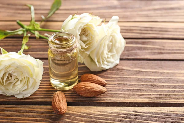 Bottiglia di olio profumato, mandorle e rose in tavola — Foto Stock