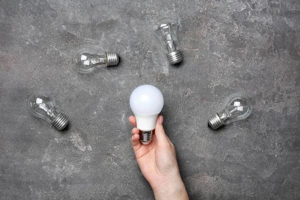 Mujer sosteniendo lámpara led cerca de bombillas incandescentes sobre fondo gris —  Fotos de Stock