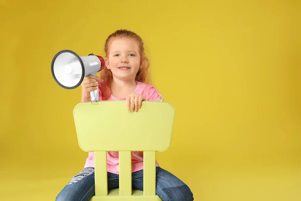 Schattig klein meisje met megafoon zit op stoel tegen een achtergrond met kleur — Stockfoto