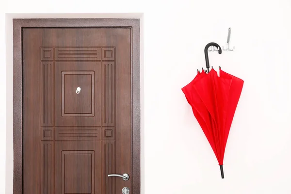 Elegante paraguas rojo colgando cerca de la puerta en la pared —  Fotos de Stock